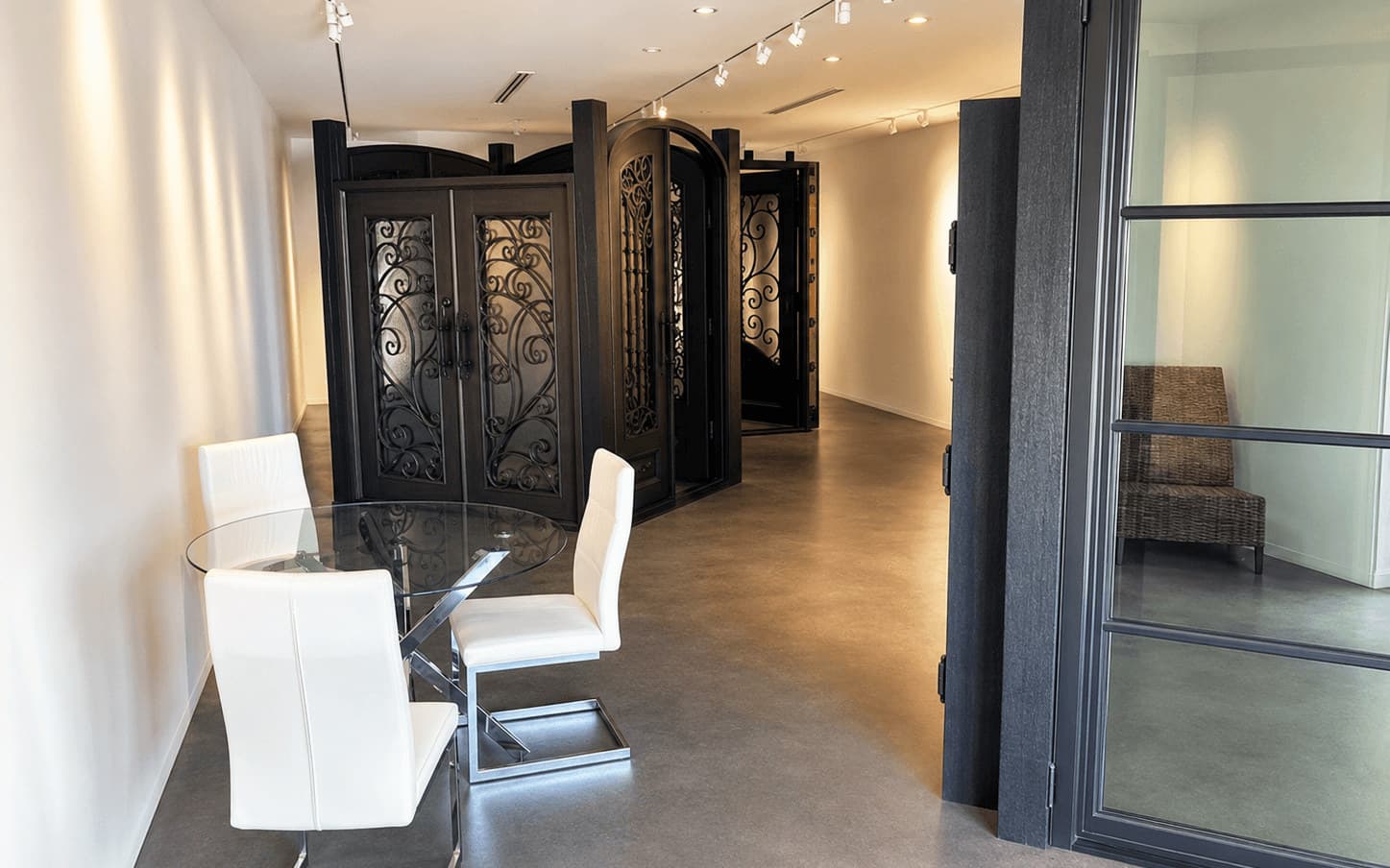 Inside the Naples showroom: full-size wrought iron entry doors with scrolled ironwork displayed beside a glass consultation table, under gallery track lighting.